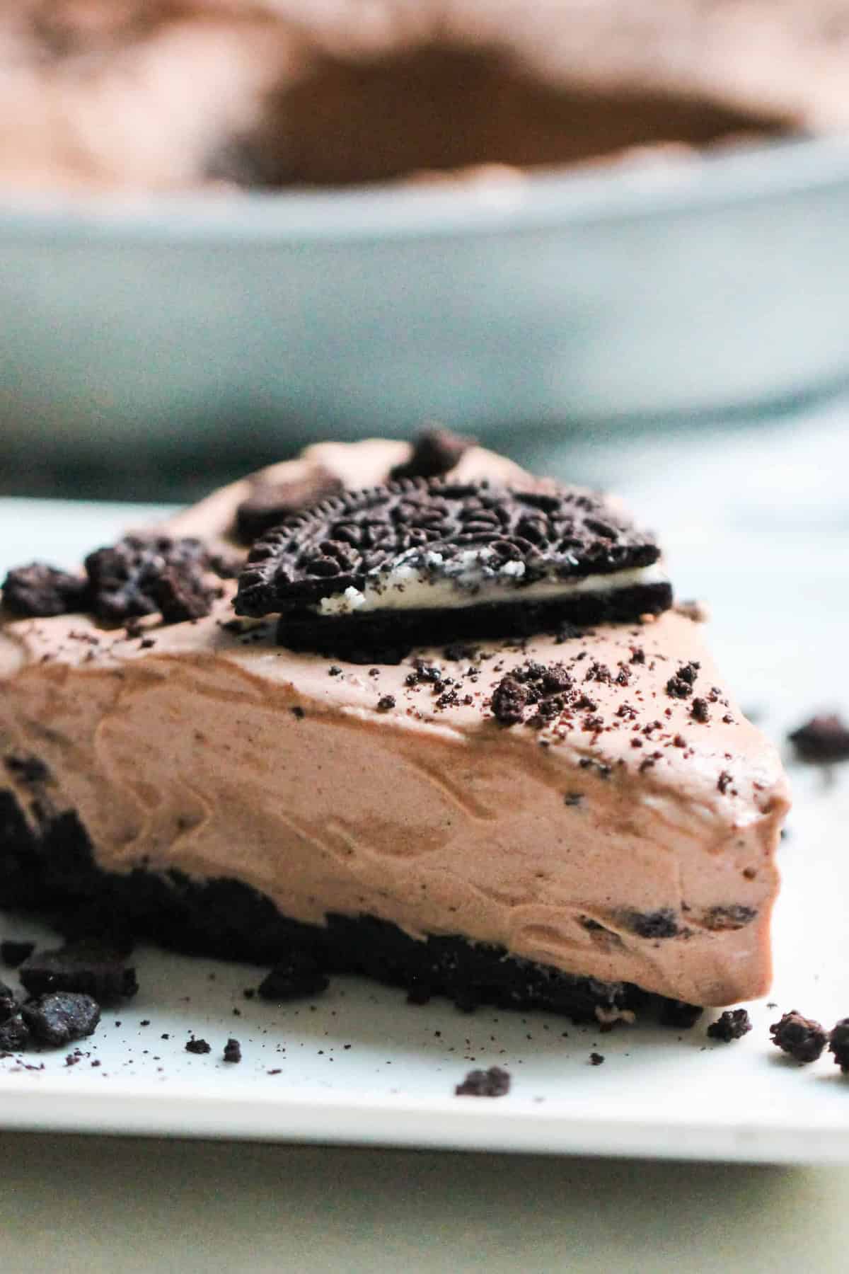 A close-up of a chocolate oreo pie topped with crumbled bits in a round metal pan on a light background with a slice missing
