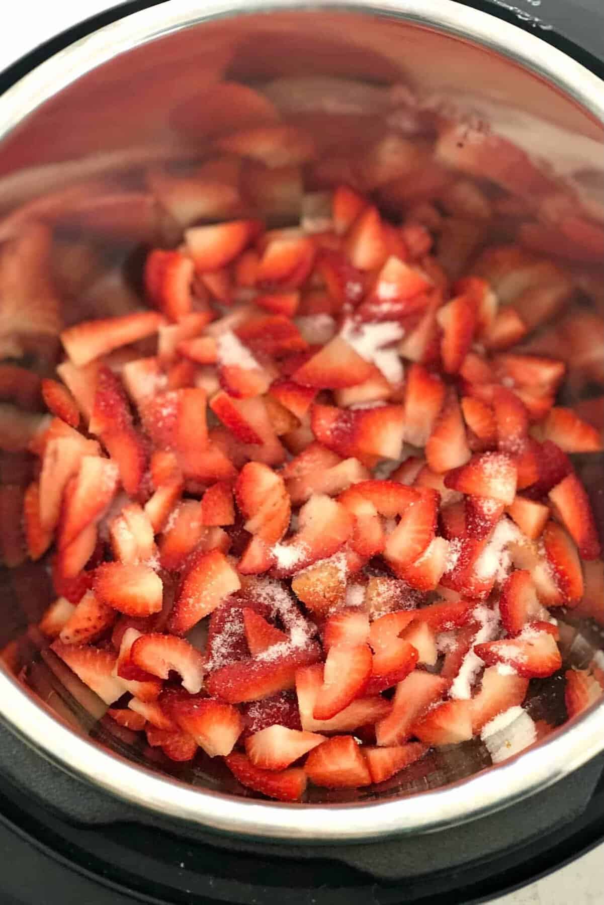 Sliced strawberries topped with sugar in a metal pot, ready for cooking.
