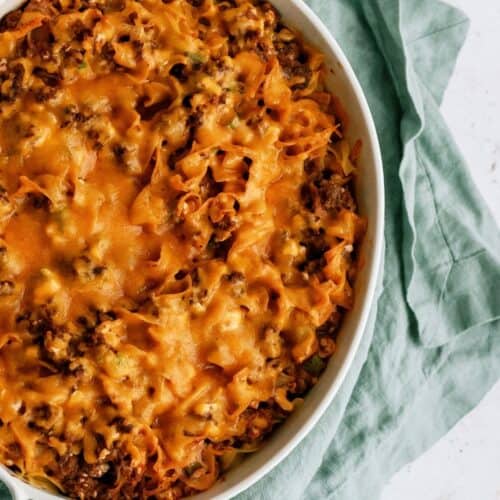 A baked casserole dish filled with noodles, ground meat, and melted cheese, placed on a light green cloth.