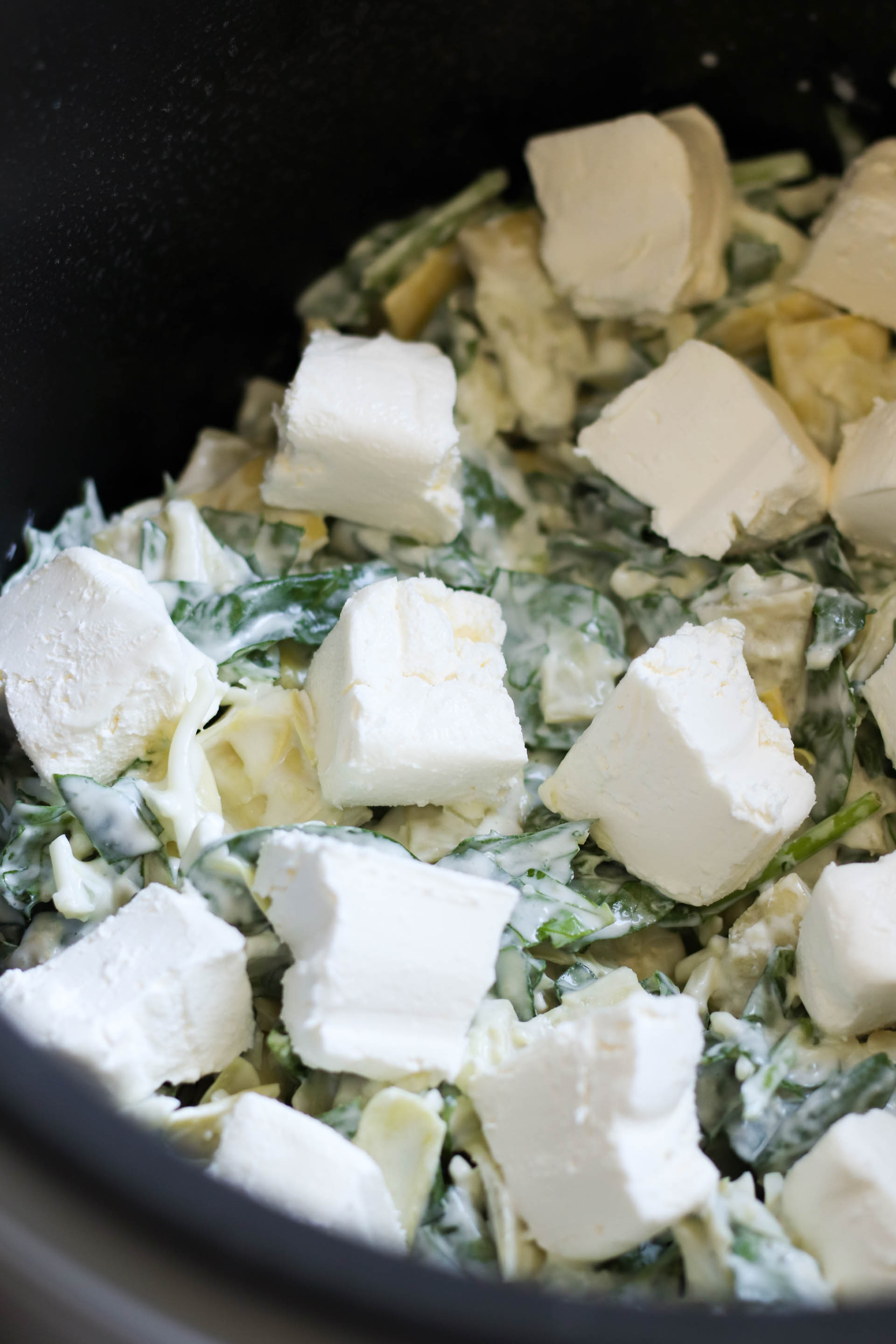 spinach artichoke dip topped with cream cheese in a slow cooker ready to be cooked