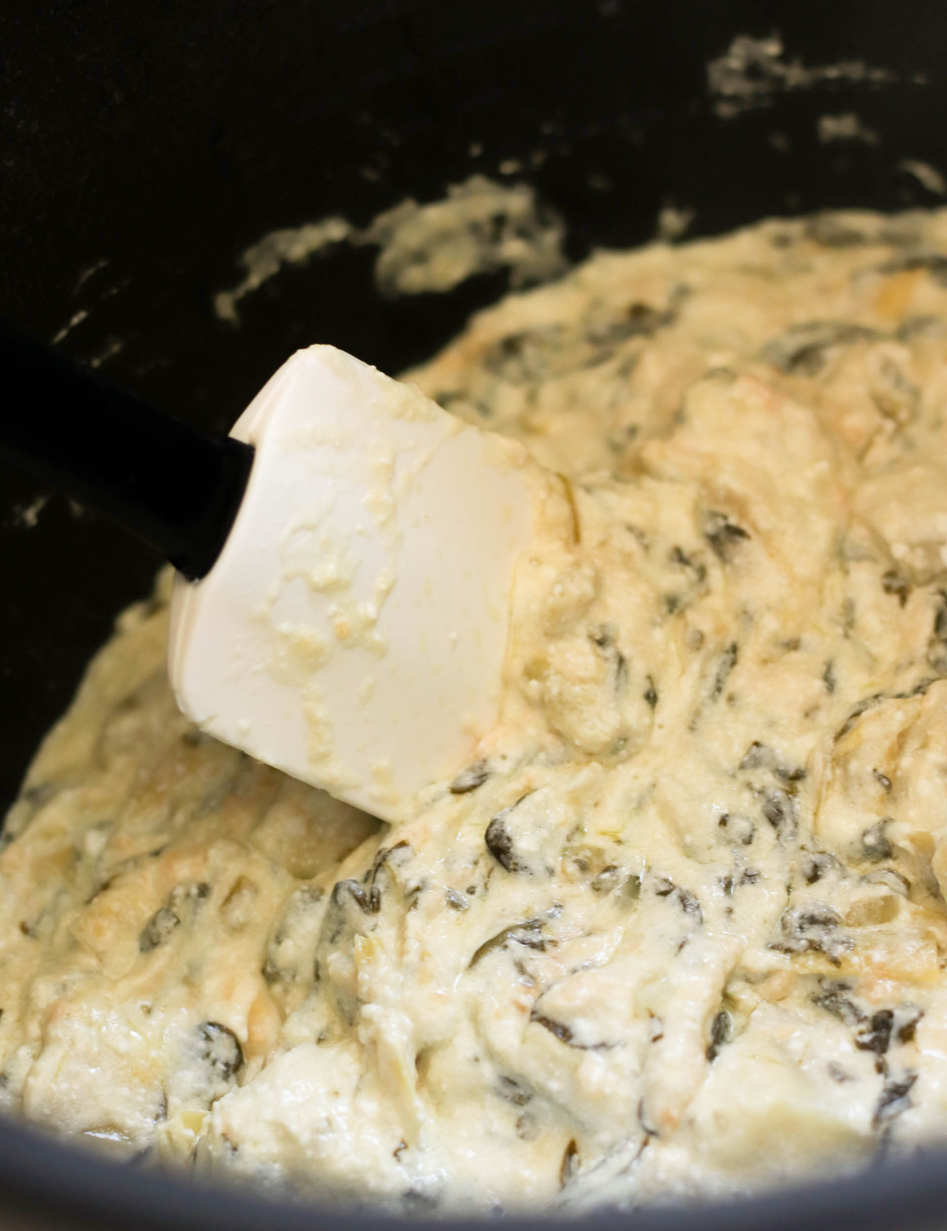 creamy spinach artichoke dip in a slow cooker being mixed with a spatula