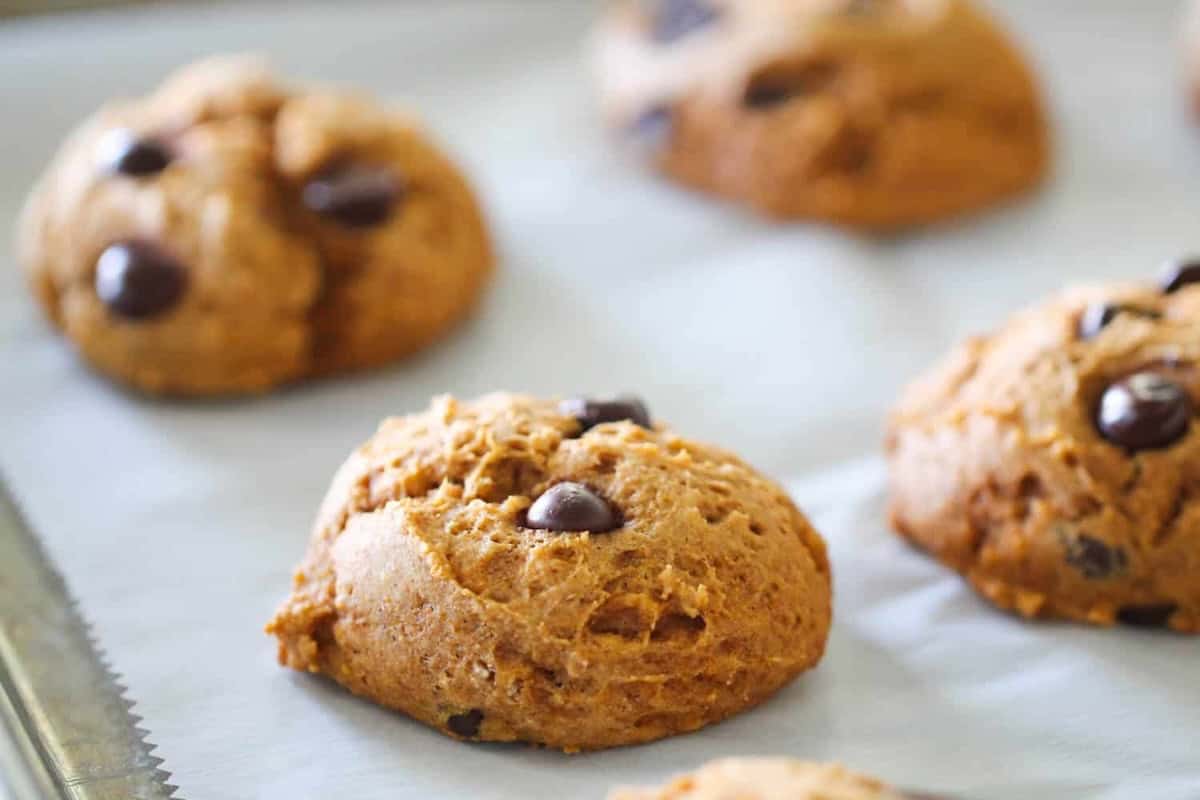 Close-up of freshly baked cookies with chocolate chips on a baking tray lined with parchment paper.