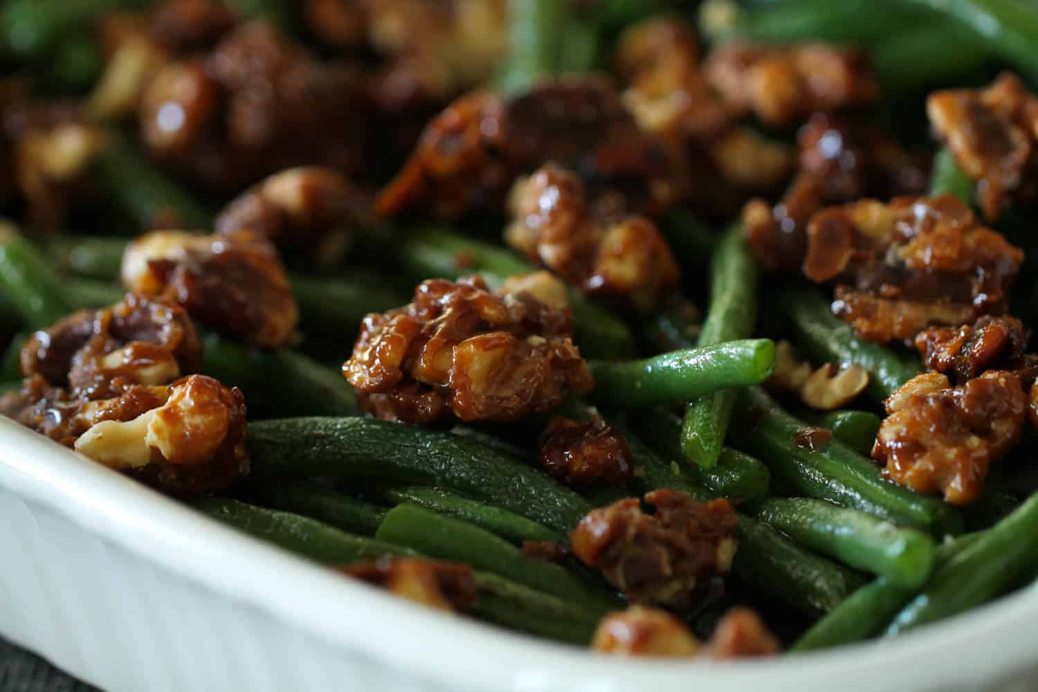 cooked green beans topped with candied pecans in a white dish