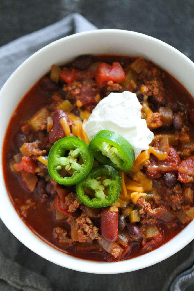 Best Homemade Chili in w white bowl topped with cheese and jalapeno