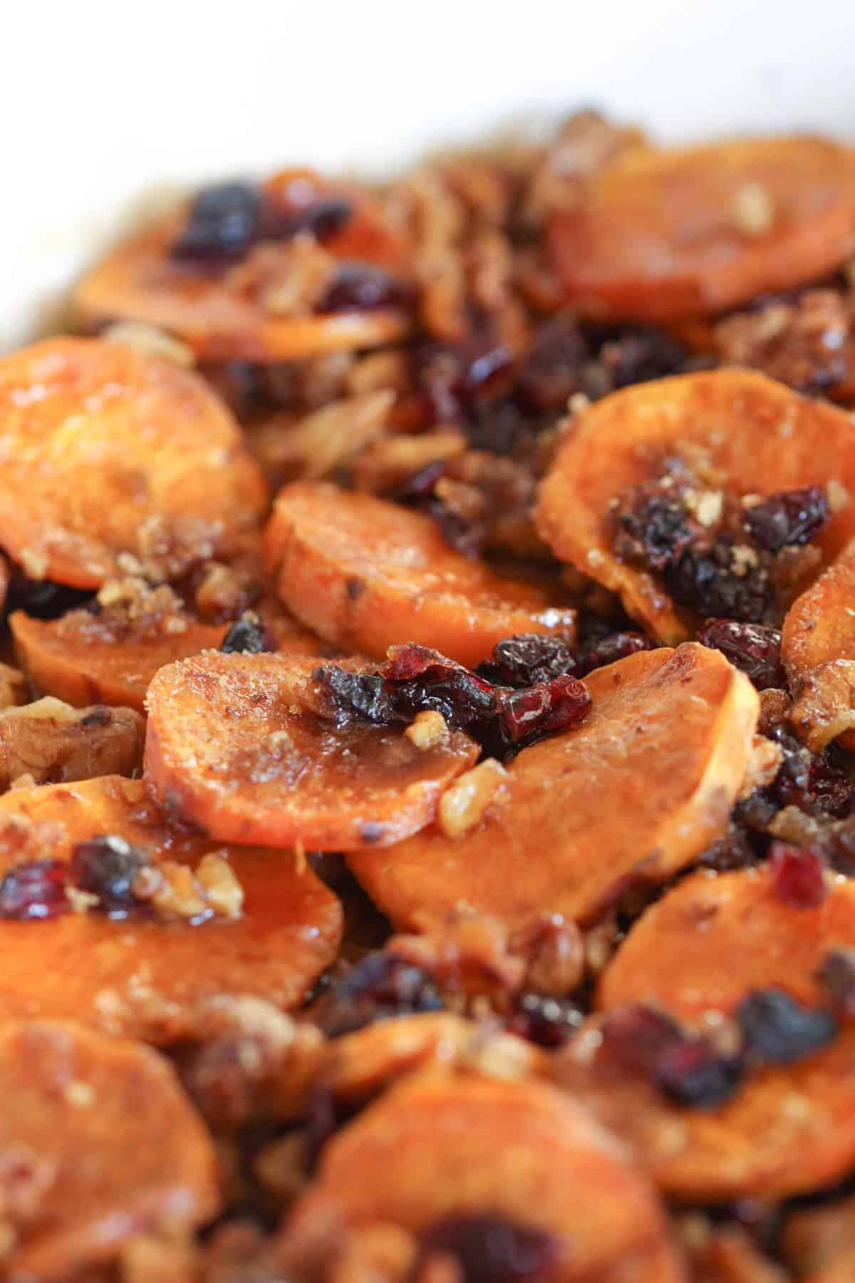 Close-up of baked sweet potato slices topped with chopped nuts and dried cranberries.