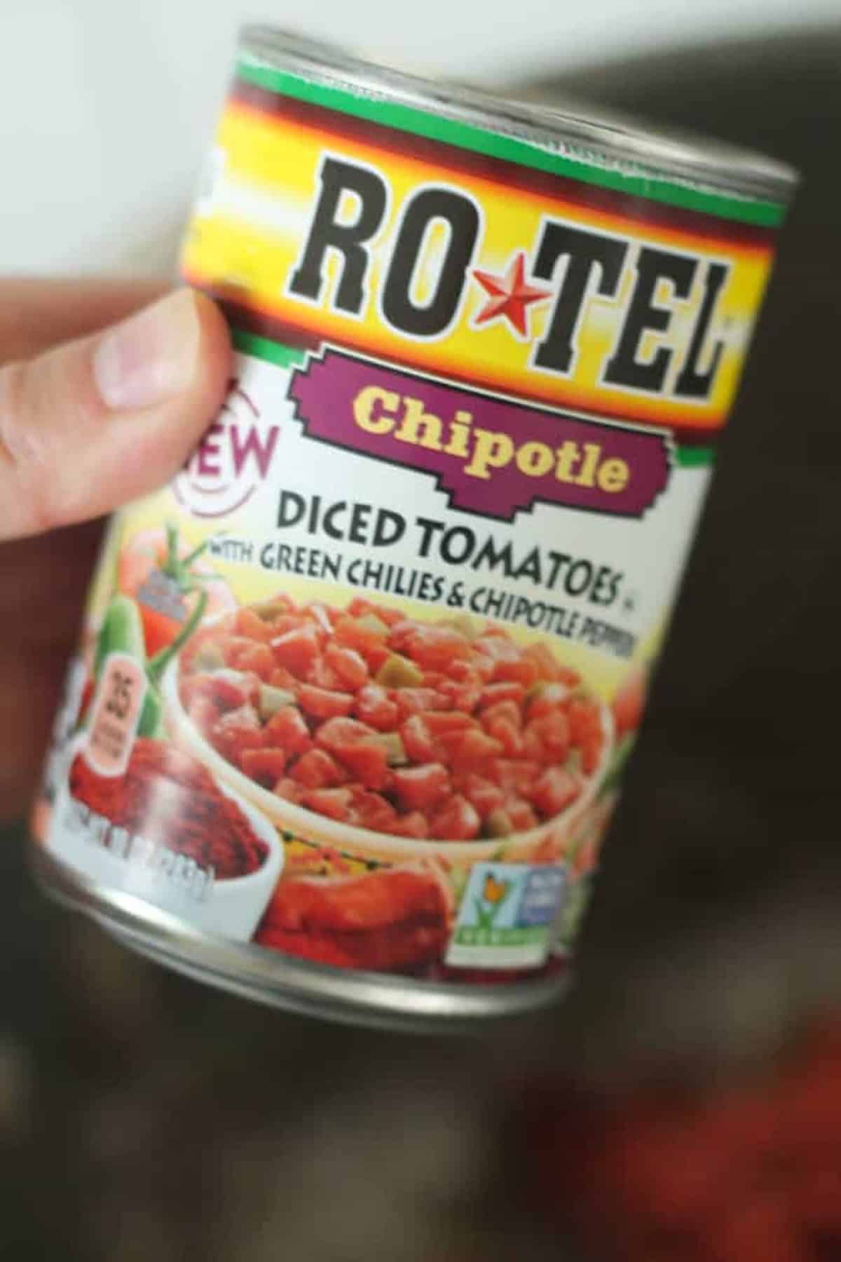 A hand holds a can of Ro-Tel Chipotle diced tomatoes with green chilies and chipotle peppers.