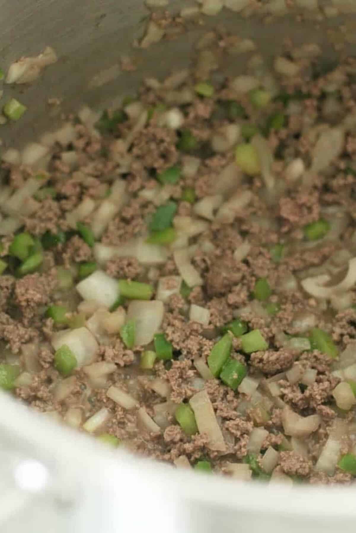 Ground beef, chopped onions, green bell peppers, and mushrooms being sautéed in a pot.