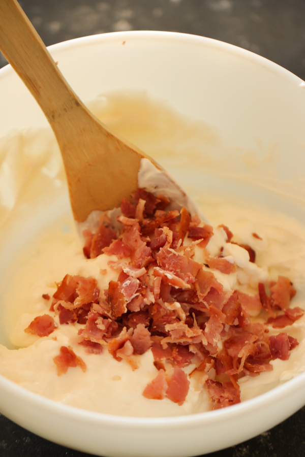 Sour cream mixture in bowl with bacon crumbles and wooden spoon