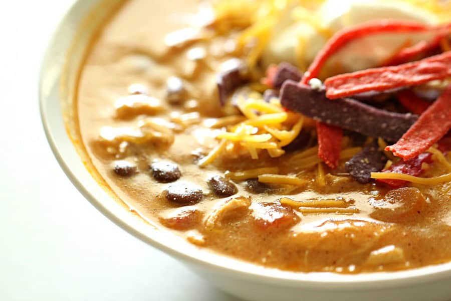 Copycat Slow Cooker Chicken Enchilada Soup in a bowl topped with cheese and tortilla strips.