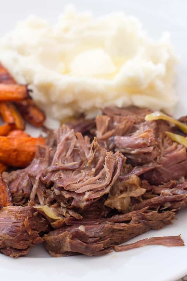 A plate of shredded beef, roasted carrots, and mashed potatoes with a pat of butter.