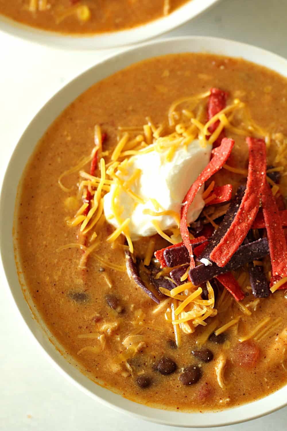 Top view of Copycat Slow Cooker Chicken Enchilada Soup in a bowl topped with cheese, sour cream and tortilla strips.