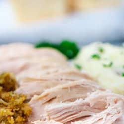 Sliced chicken breast served with stuffing and mashed potatoes, garnished with parsley, on a white plate.