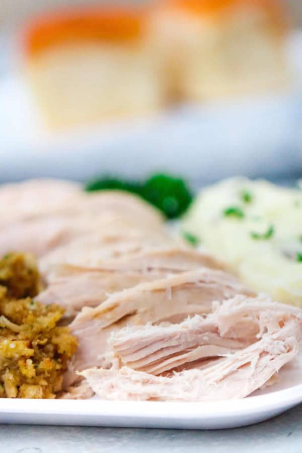 Sliced chicken breast served with stuffing and mashed potatoes, garnished with parsley, on a white plate.
