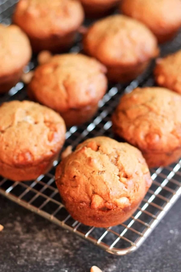 A cooling rack with several freshly baked muffins with a golden-brown top, resting on a dark surface.