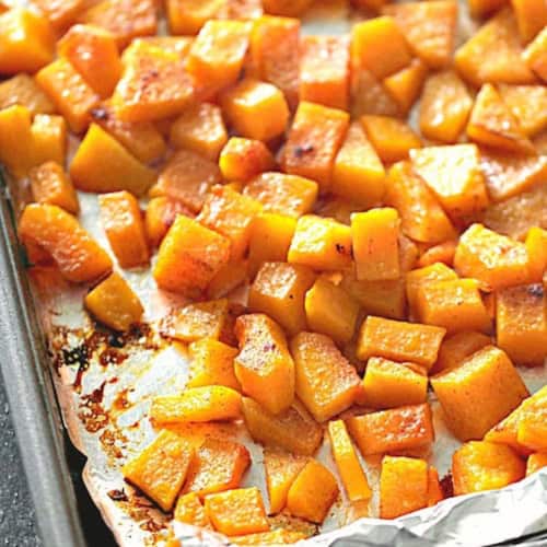 Cubed butternut squash roasted on a foil-lined baking sheet, seasoned and browned around the edges.