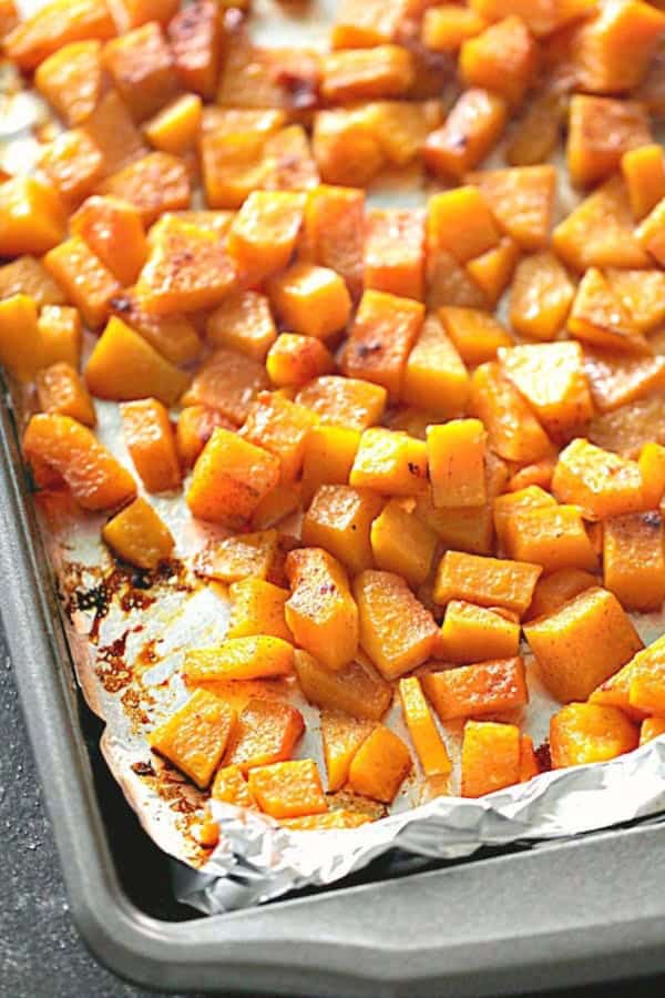 Cubed butternut squash roasted on a foil-lined baking sheet, seasoned and browned around the edges.