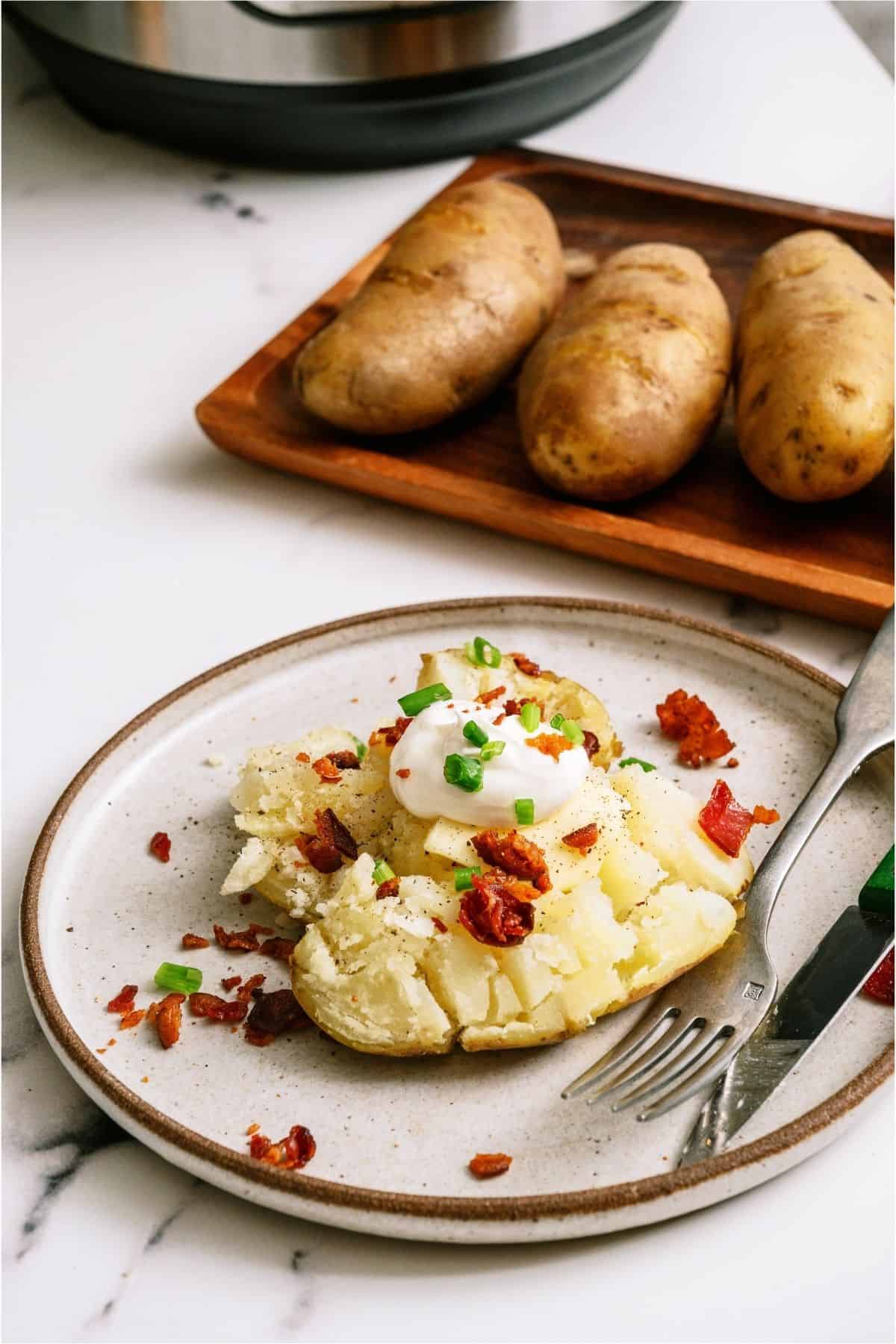 A plate with an Instant Pot Baked Potato with a tray of Instant Pot Baked Potatoes in the background.
