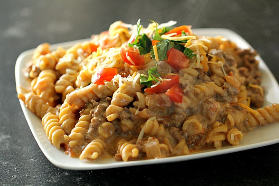 cheesy beef taco pasta on a plate topped with tomatoes and cilantro