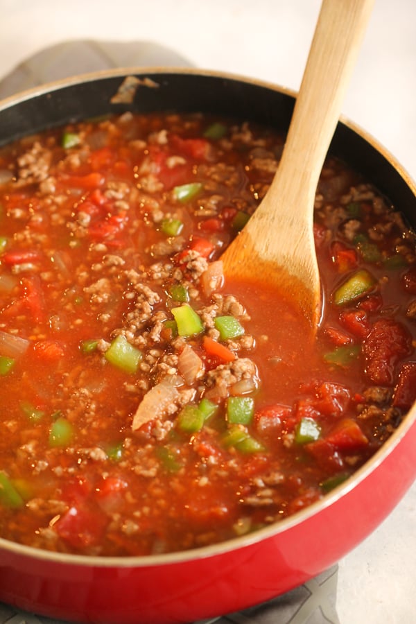 Meat, broth, tomato sauce and peppers in a pan with a wooden spoon