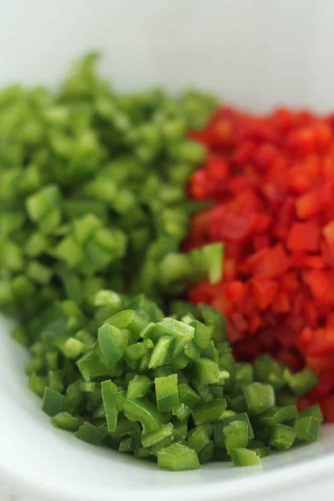 Chopped green and red peppers with chopped jalapeno peppers on a white plate