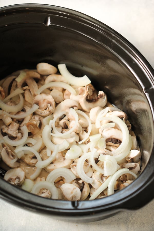 Sliced onions and mushrooms in the bottom of slow cooker