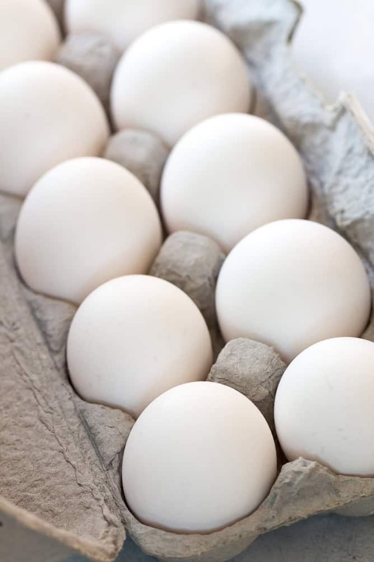 A carton of ten white eggs in a cardboard egg tray.