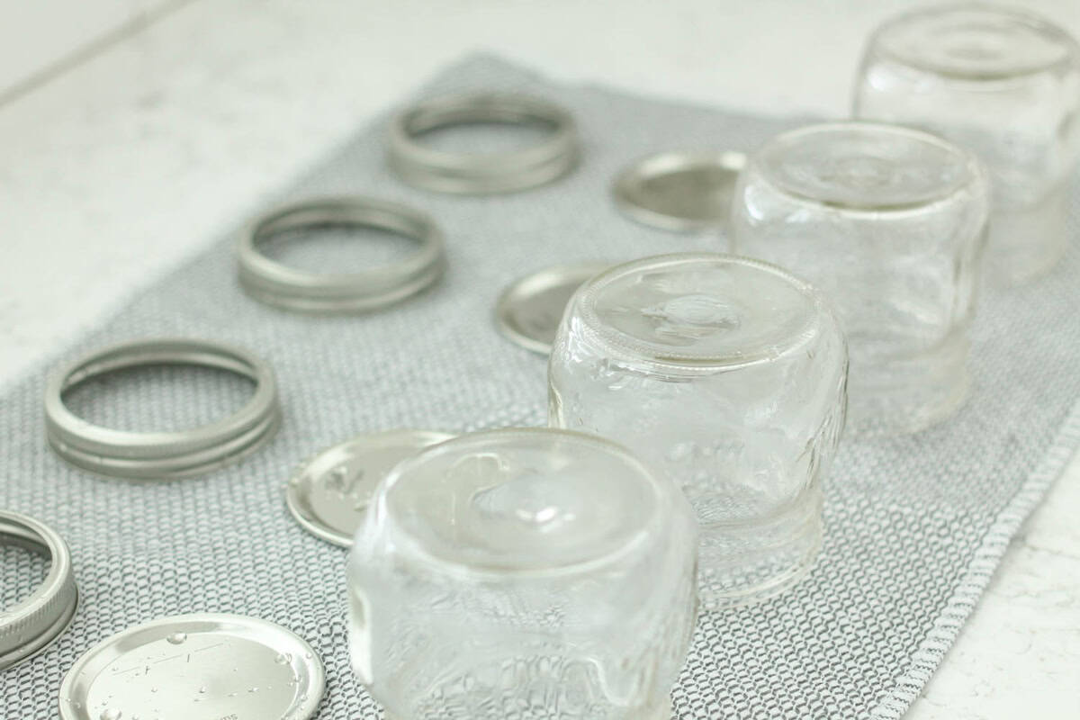Four clean glass jars and several metal lids are drying upside down on a gray towel.