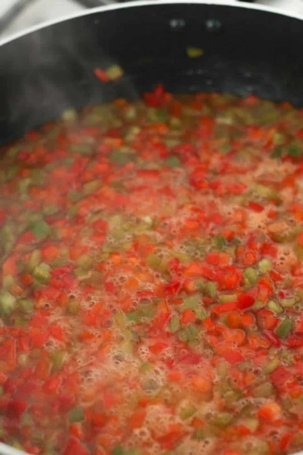 Diced red and green bell peppers simmer in a pot with bubbling liquid, producing steam.