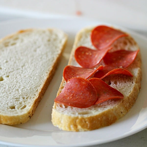 2 pieces of bread on a plate, one topped with pepperoni slices