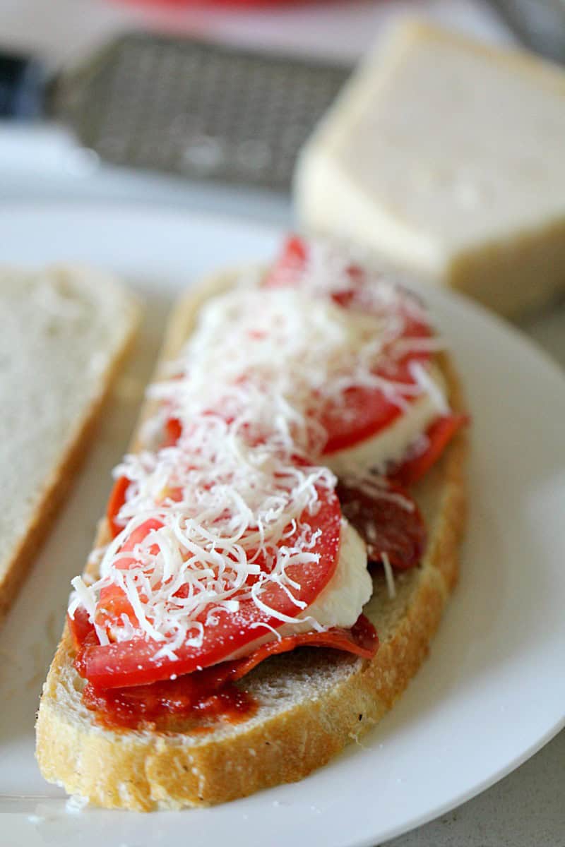 2 pieces of bread on a plate, one topped with pepperoni slices, marinara and cheese