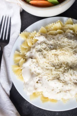A plate of bowtie pasta topped with a creamy white sauce and grated cheese, with a fork on a napkin beside the plate.