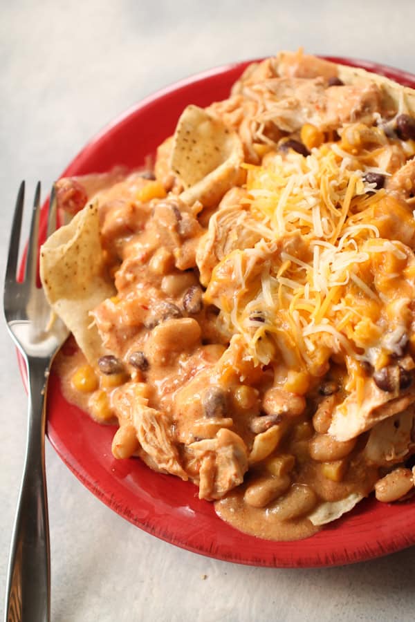 Slow Cooker Creamy Bean and Salsa Chicken on top of nachos on a plate