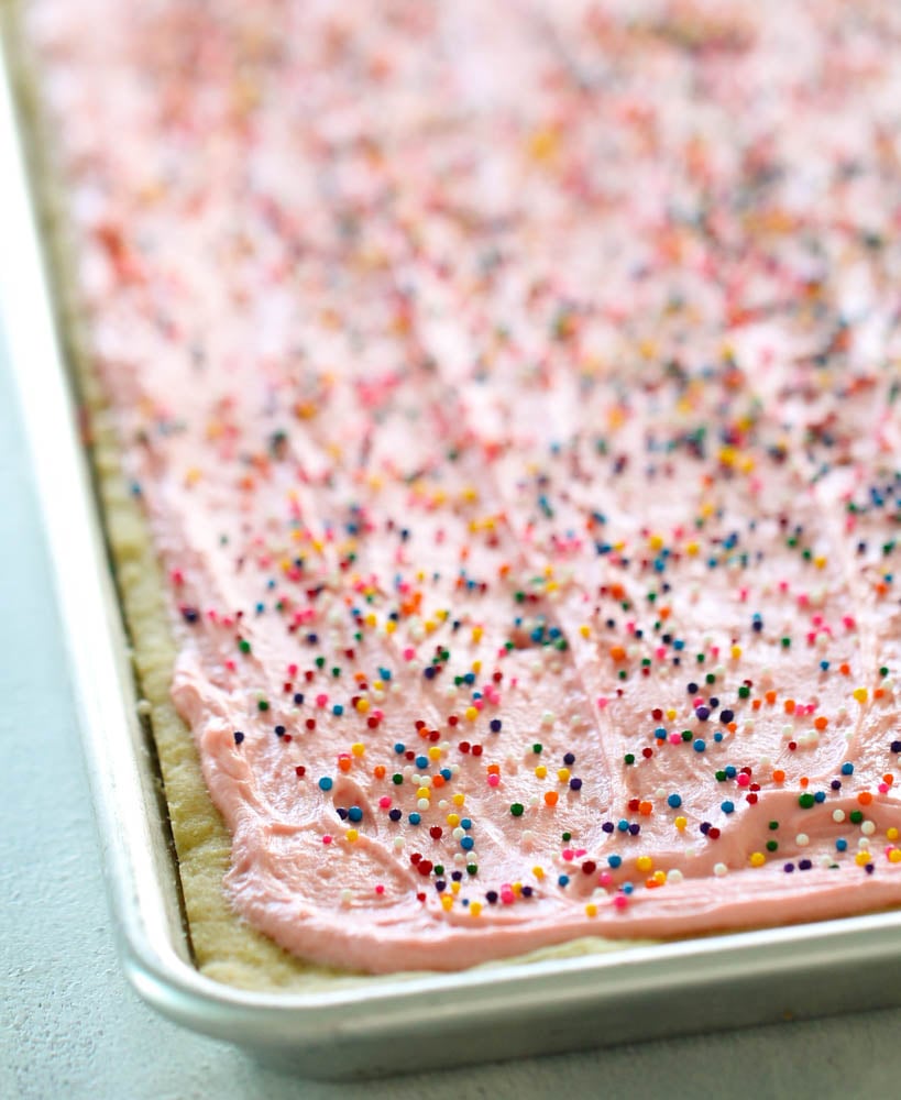 freshly frosted sugar cookie bars in a sheet pan with sprinkles on top