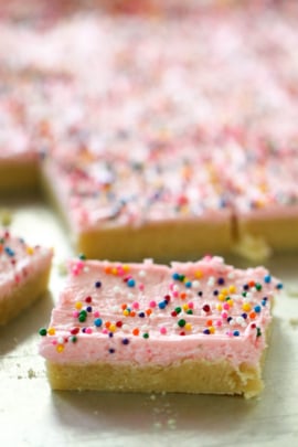 Frosted Sugar Cookie Bars cut into squares and topped with rainbow sprinkles