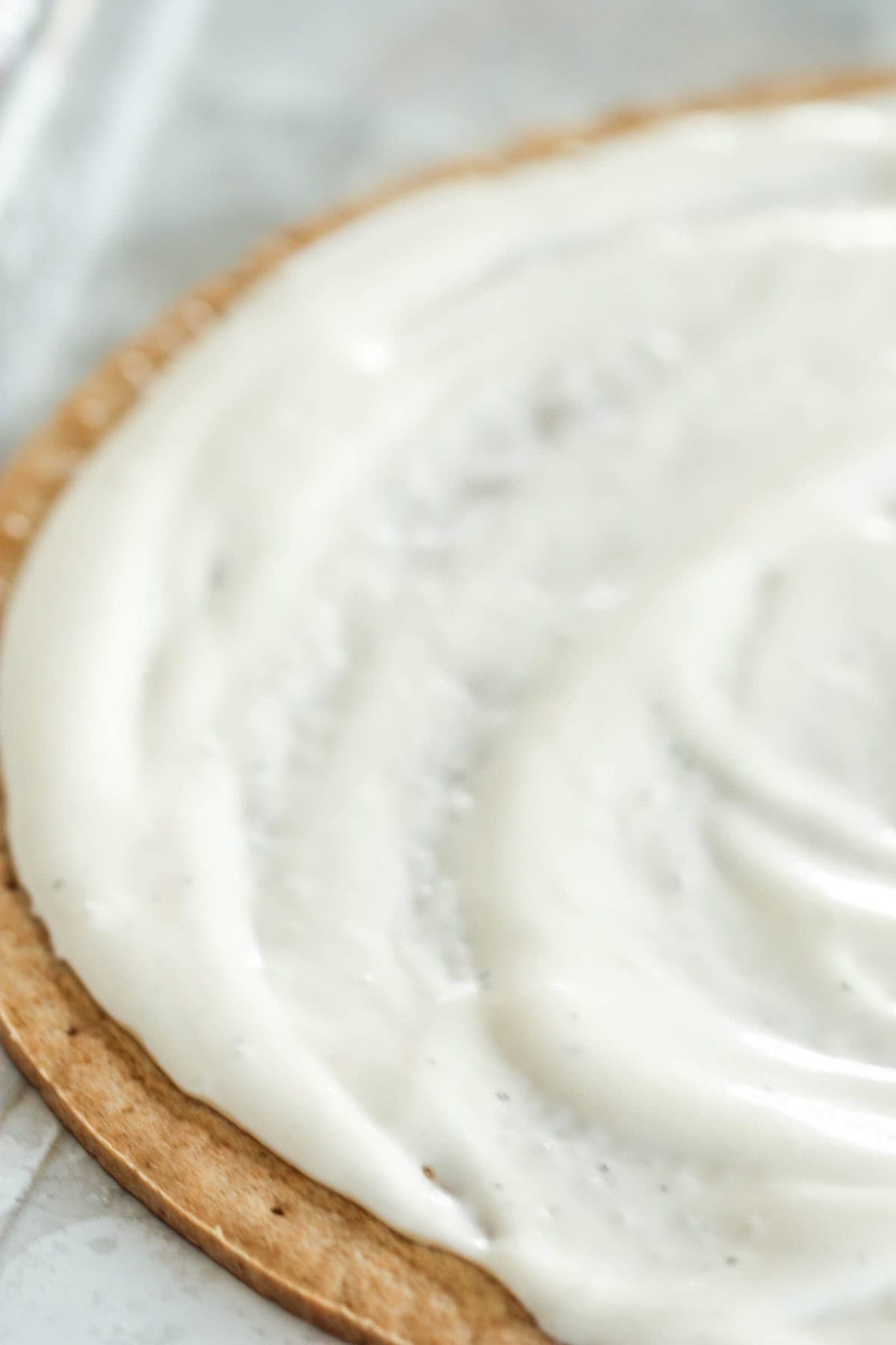 A close-up of a round crust with a thick, even layer of white creamy spread on top.