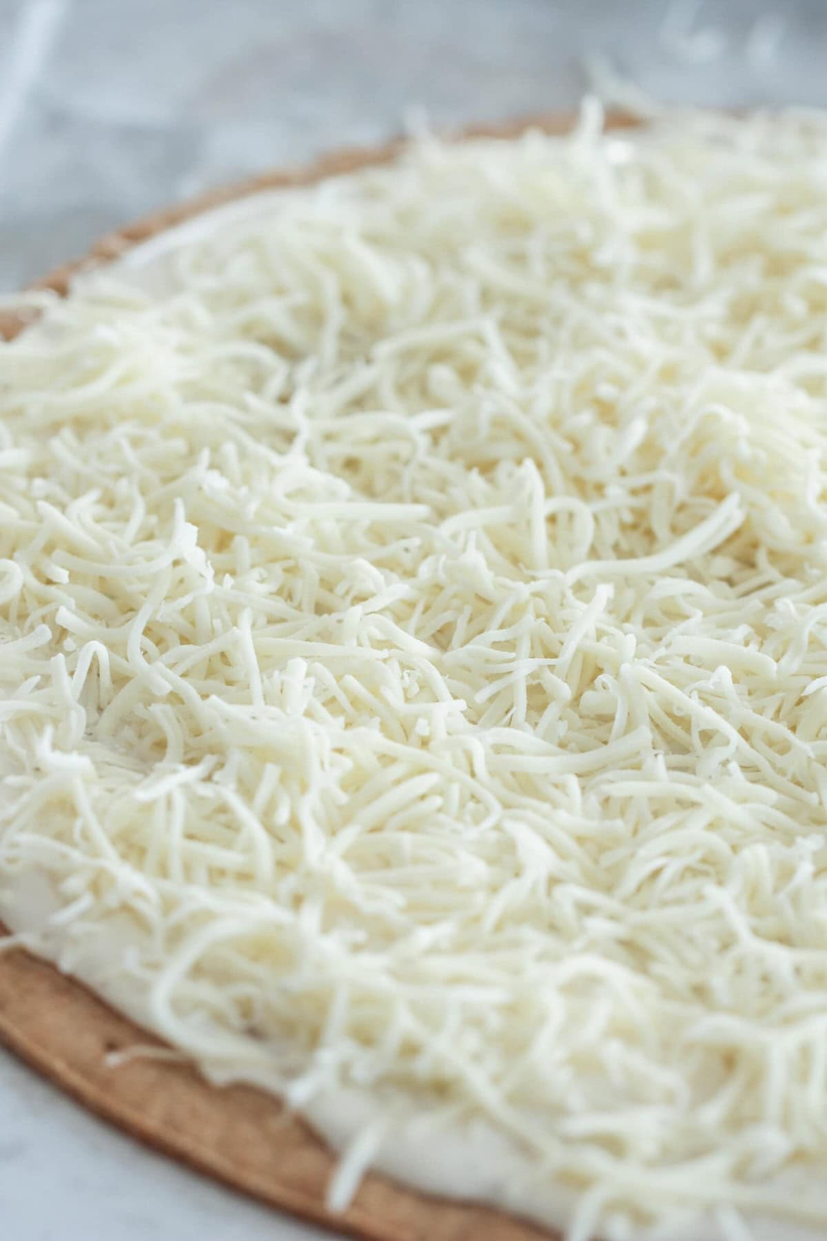 A pizza crust topped with a thick layer of shredded mozzarella cheese, ready to be baked.