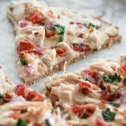 A rectangular pizza slice topped with shredded chicken, red onions, sundried tomatoes, spinach, and melted cheese on a baking tray.
