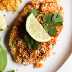 Breaded tilapia garnished with lime slices and cilantro, served on a white plate with a side of rice and greens.