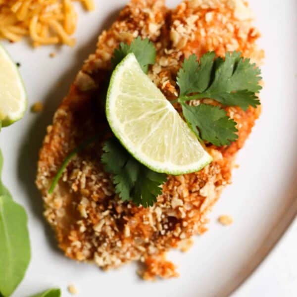 Breaded tilapia garnished with lime slices and cilantro, served on a white plate with a side of rice and greens.