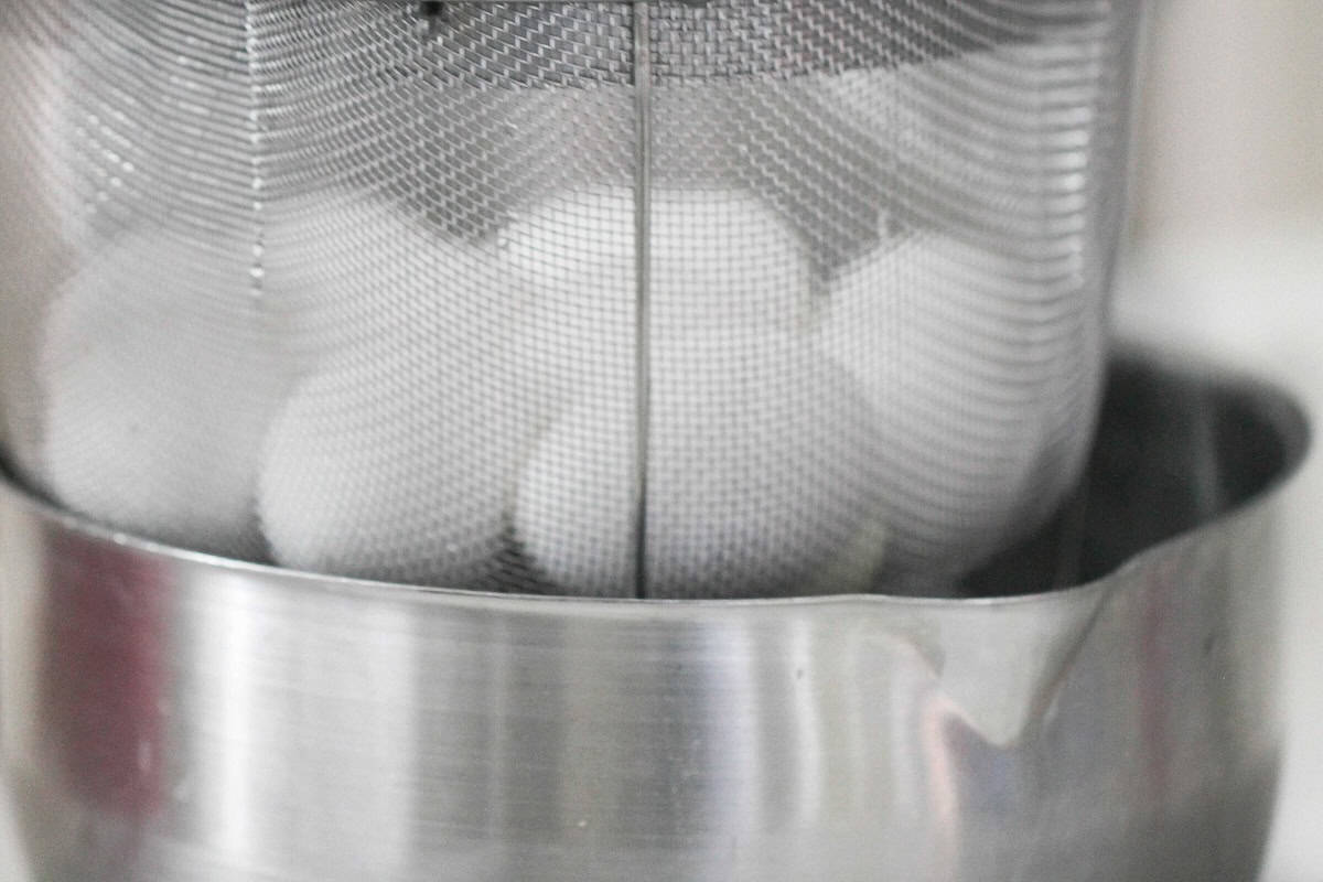 A stainless steel colander with white eggs inside is placed over a stainless steel mixing bowl.