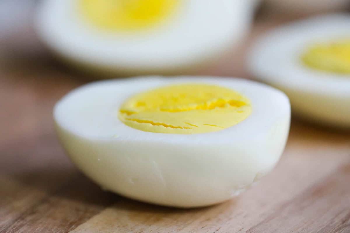 Close-up of a halved hard-boiled egg on a wooden surface, showing a bright yellow yolk surrounded by firm white egg whites.