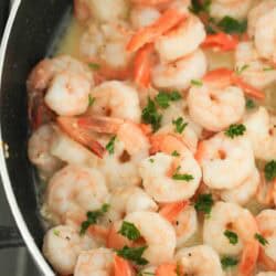 Shrimp sautéing in a pan with a light sauce and garnished with chopped parsley.