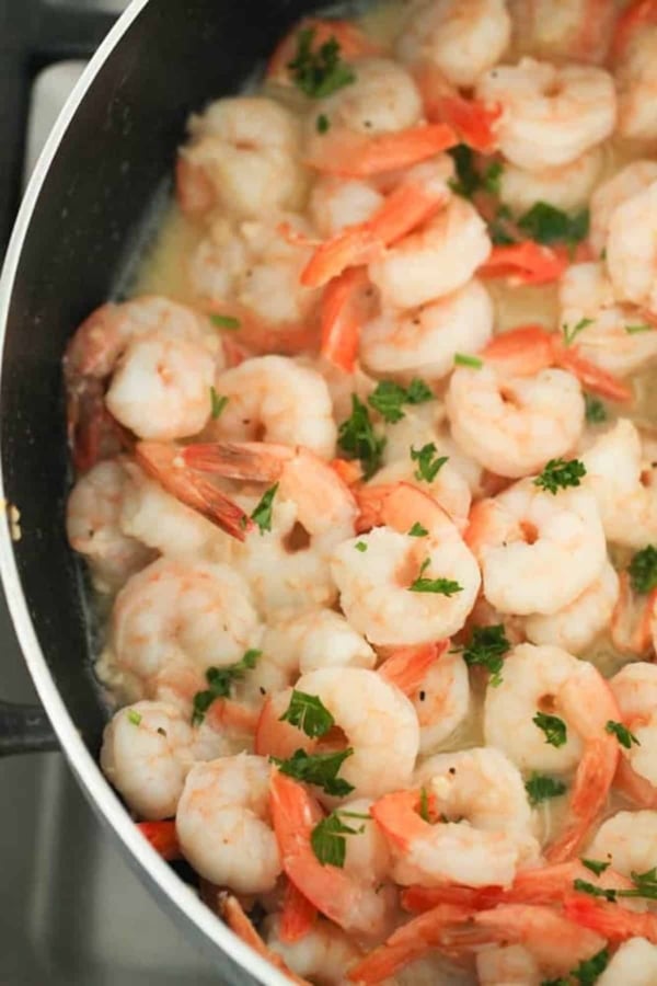 Shrimp sautéing in a pan with a light sauce and garnished with chopped parsley.