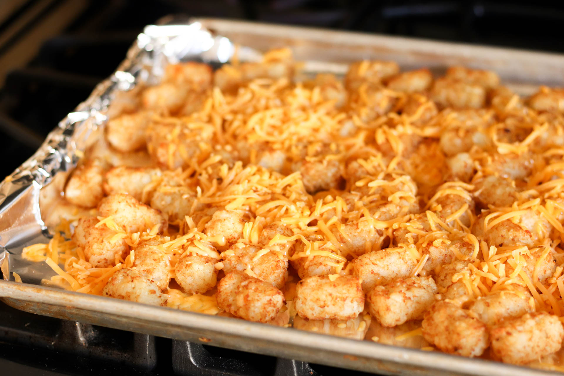 Tater tots on sheet pan covered with shredded cheese