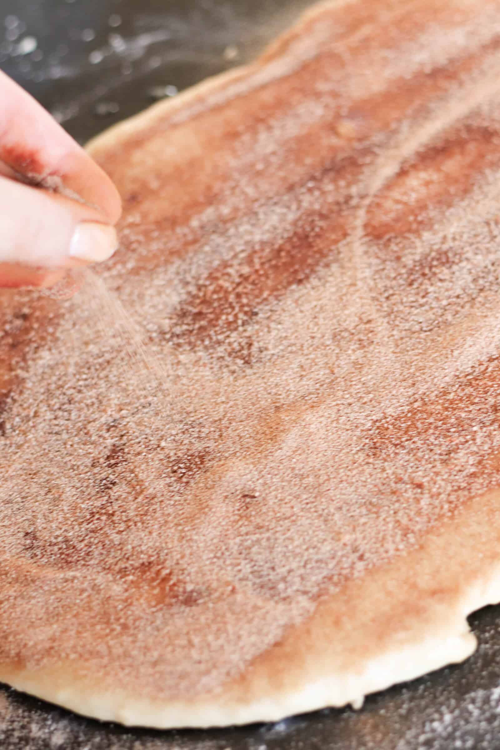 Bread dough rolled out with cinnamon and sugar sprinkled on top