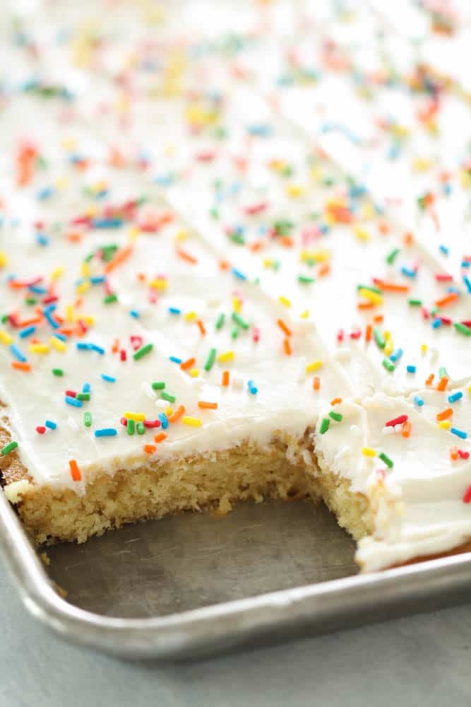 White Texas Sheet Cake frosted with sprinkles in a sheet pan with a corner piece missing.