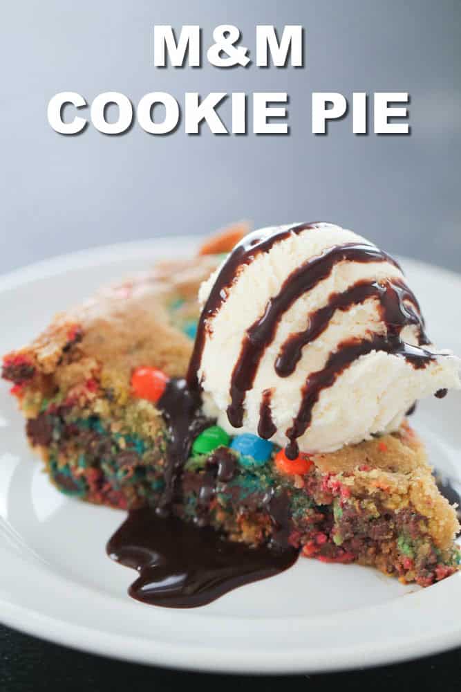 M&M Cookie Pie slice on a white plate with ice cream and chocolate sauce