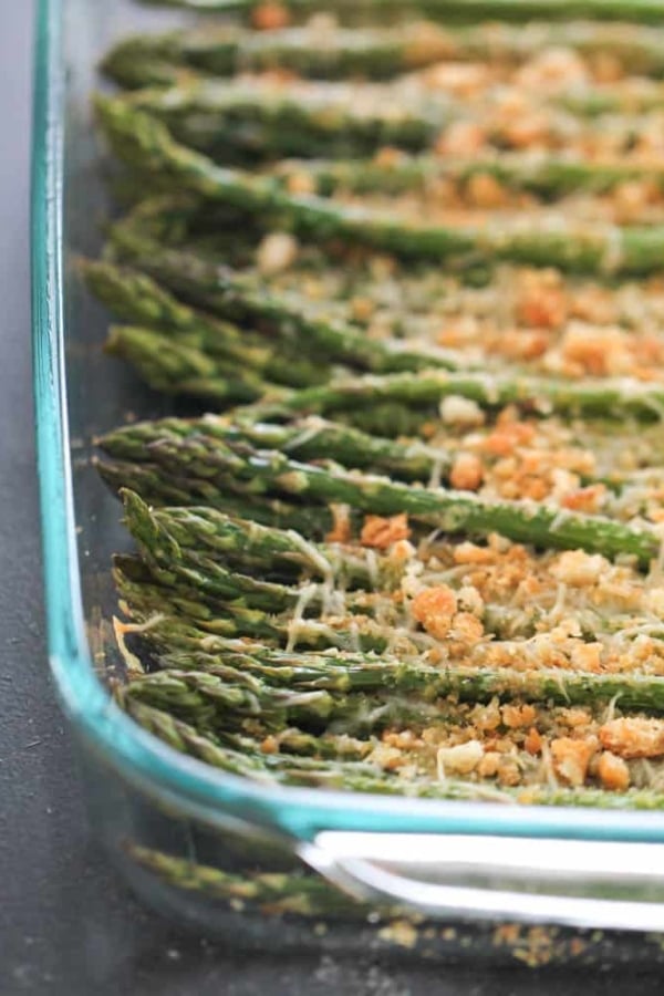 Glass dish containing roasted asparagus spears topped with breadcrumbs and grated cheese.