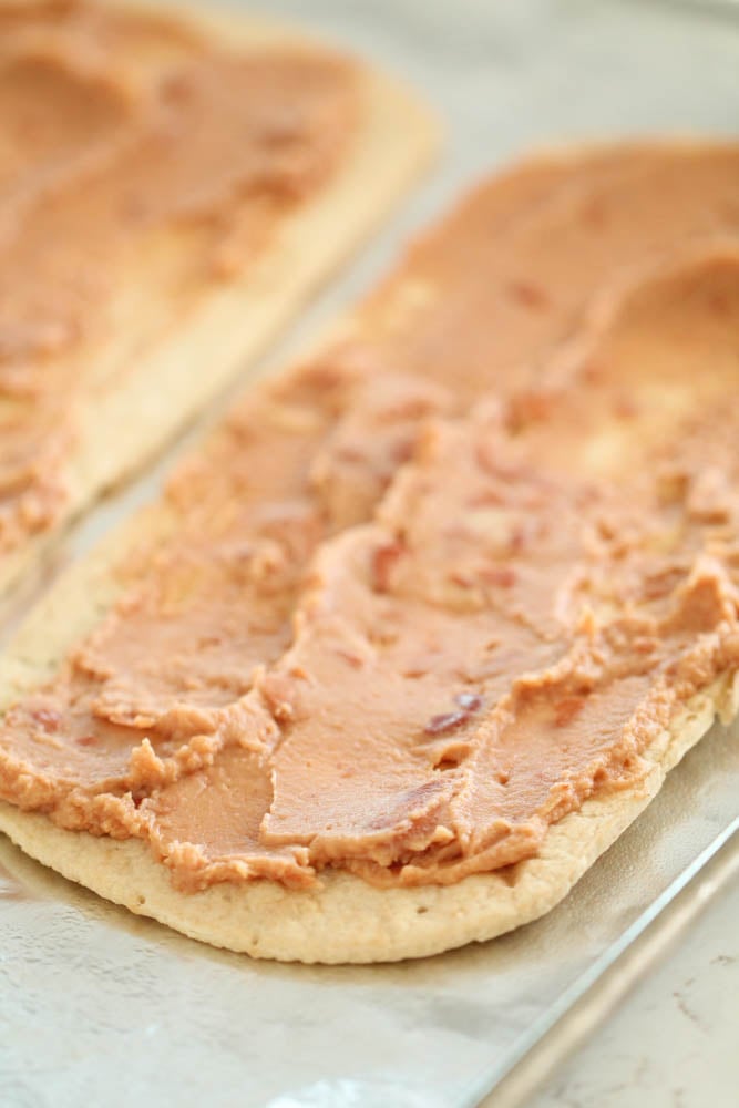 flatbread spread with refried beans on a baking sheet