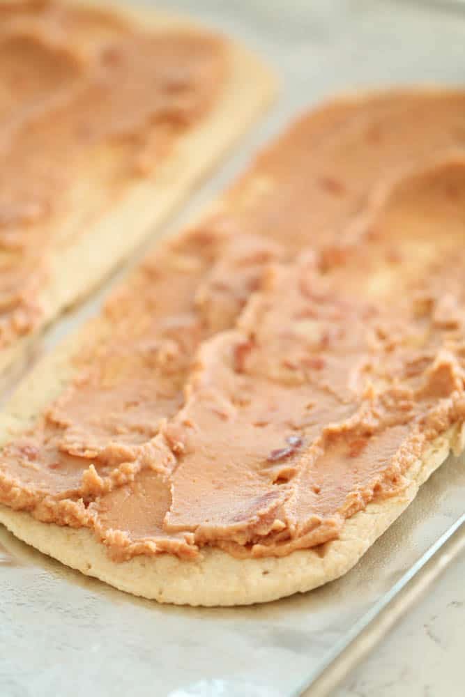 flatbread spread with refried beans on a baking sheet